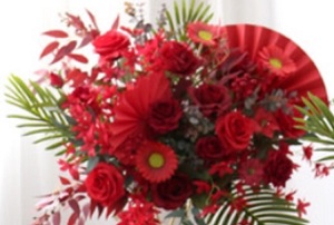 Red roses gerberas carnations with golden cane palm leaves tropical foliage in basket arrangement