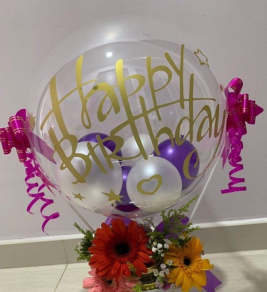 Clear Balloon stuffed with balloons and happy birthday print with basket of gerberas